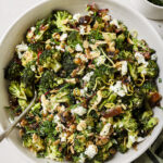 roasted broccoli and chickpea salad topped with vegan feta, fresh mint, and slivered almonds. The salad is in a white bowl with a silver fork in it.