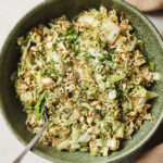 image of nappa cabbage salad with ramen noodles in a green bown with a fork in it. Sprinkled with fresh green onion and cilantro. There is a brown kitchen towel to the left side of the bowl.