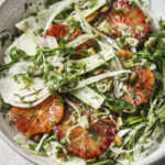Blood orange and fennel salad in a grey/white bowl with lemon dressing on top, sprinkled with fresh herbs and pistachio.
